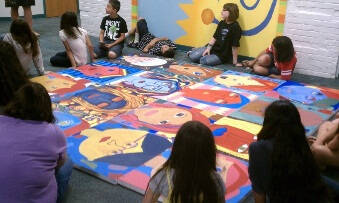 Children around a large painting of faces.